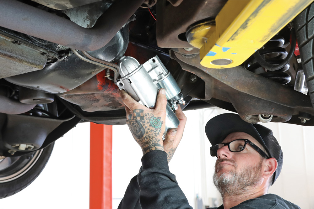 mechanic works beneath raised car to reach bolt locations