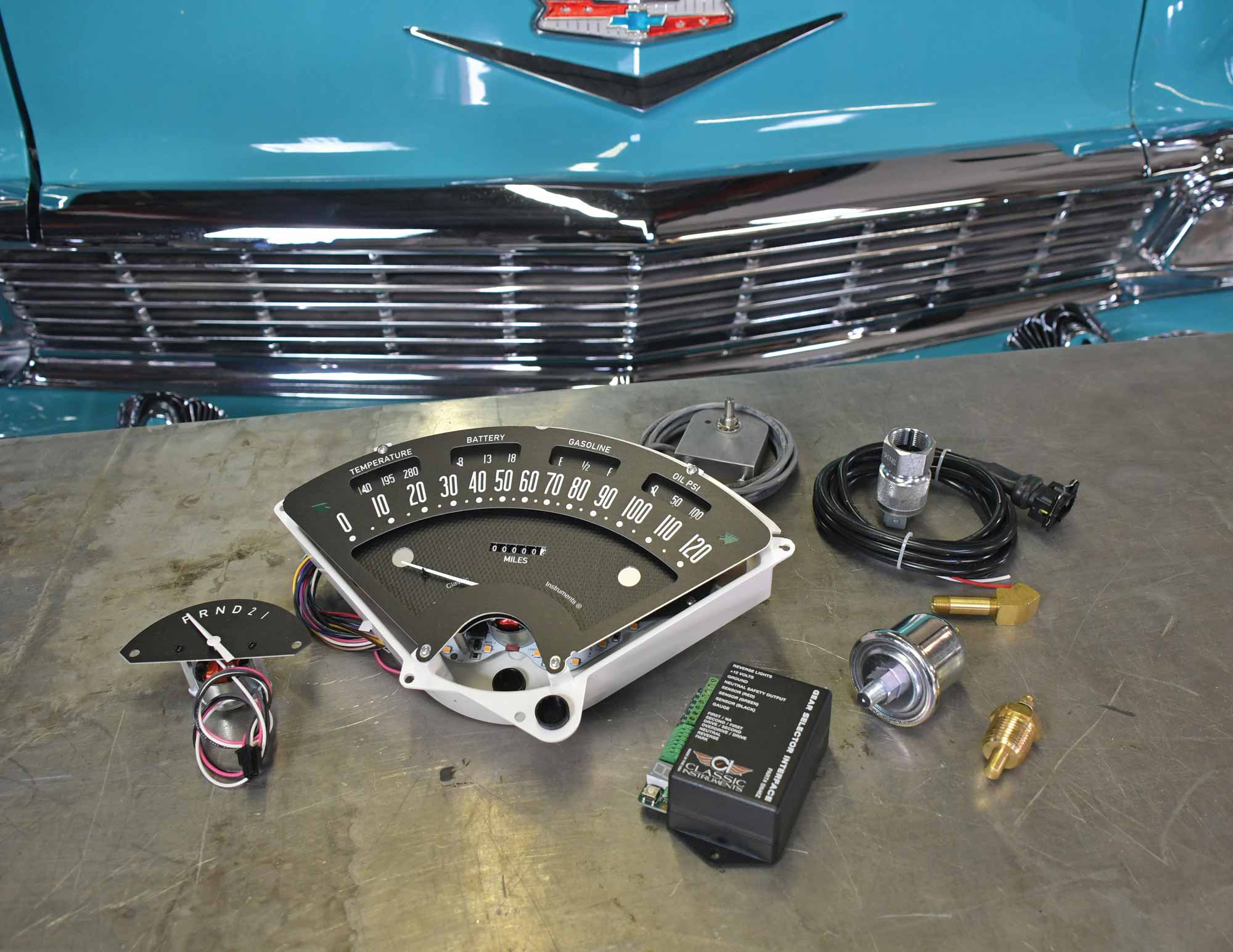 Parts of Classic Instruments' Bel Era III Dash on a table in front of the fender of a 1956 Chevrolet