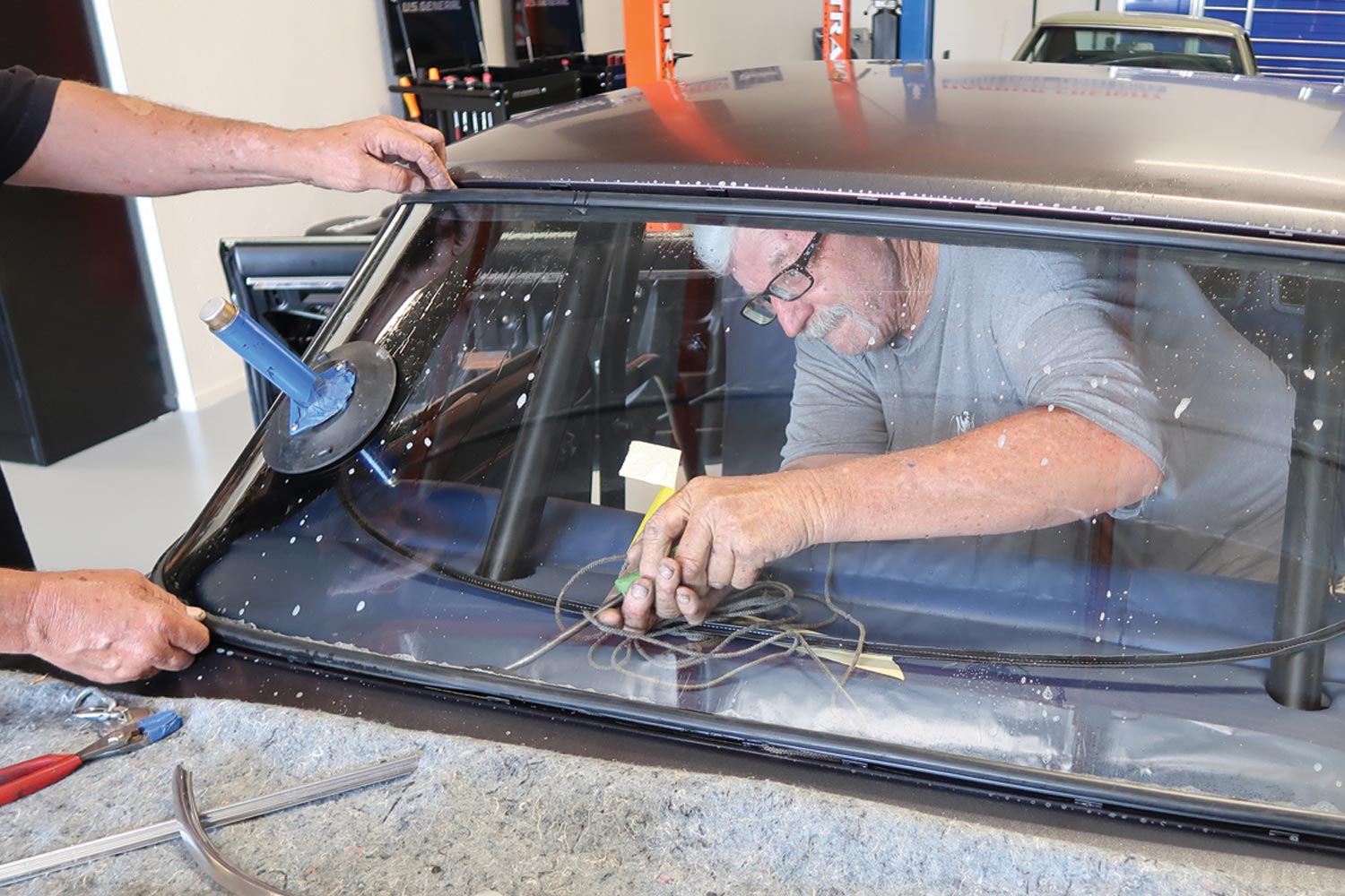 one of the two mechanics pulls the cord out of the gasket, a process often called “roping in” the glass