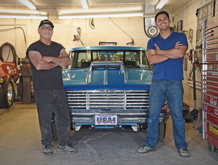 two men standing in front of a Blue '63 Chevy II