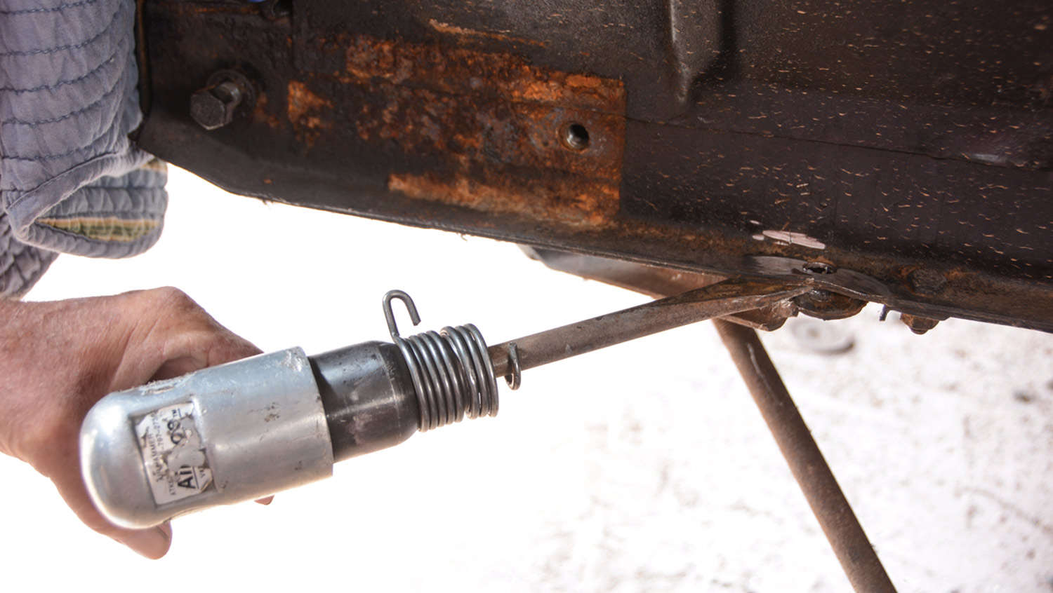 mechanic uses an air chisel to remove the rivets that hold the strut rod brackets to the framerails
