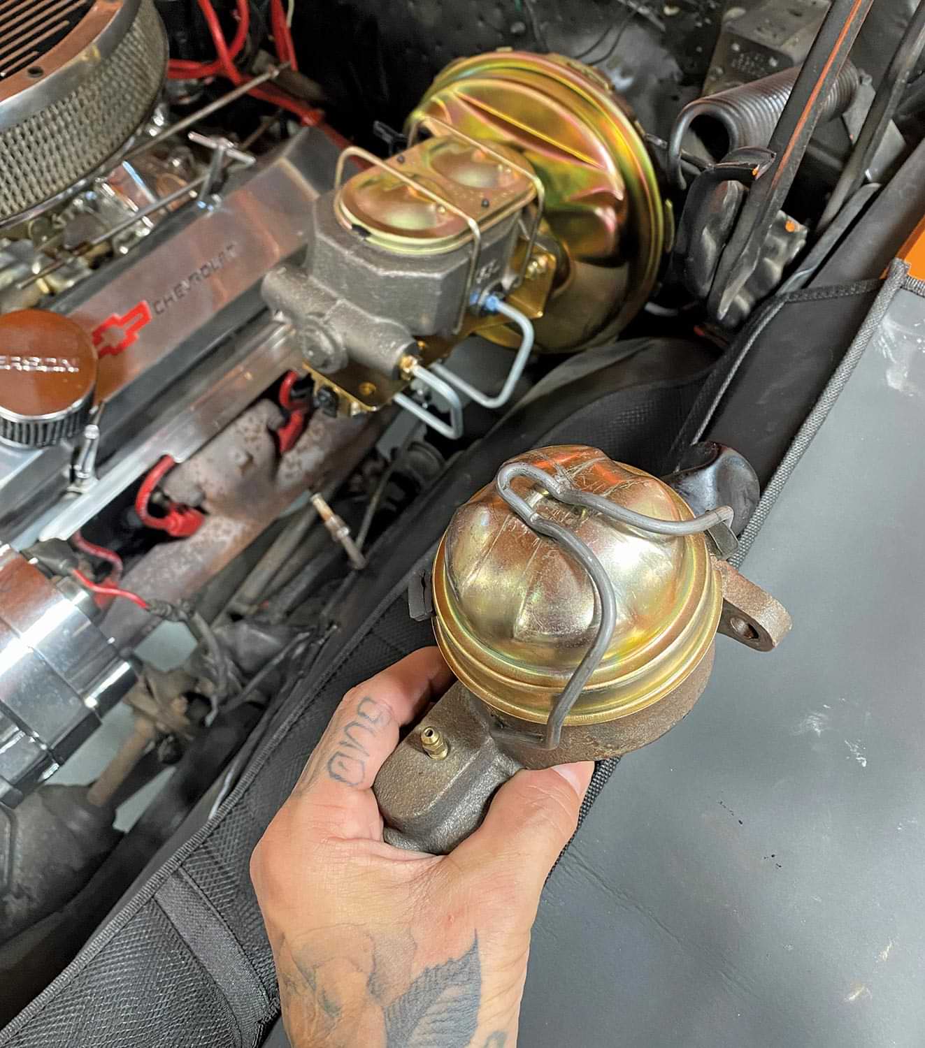 mechanic holds the old single-reservoir style master cylinder in hand with the new updated one installed in the background