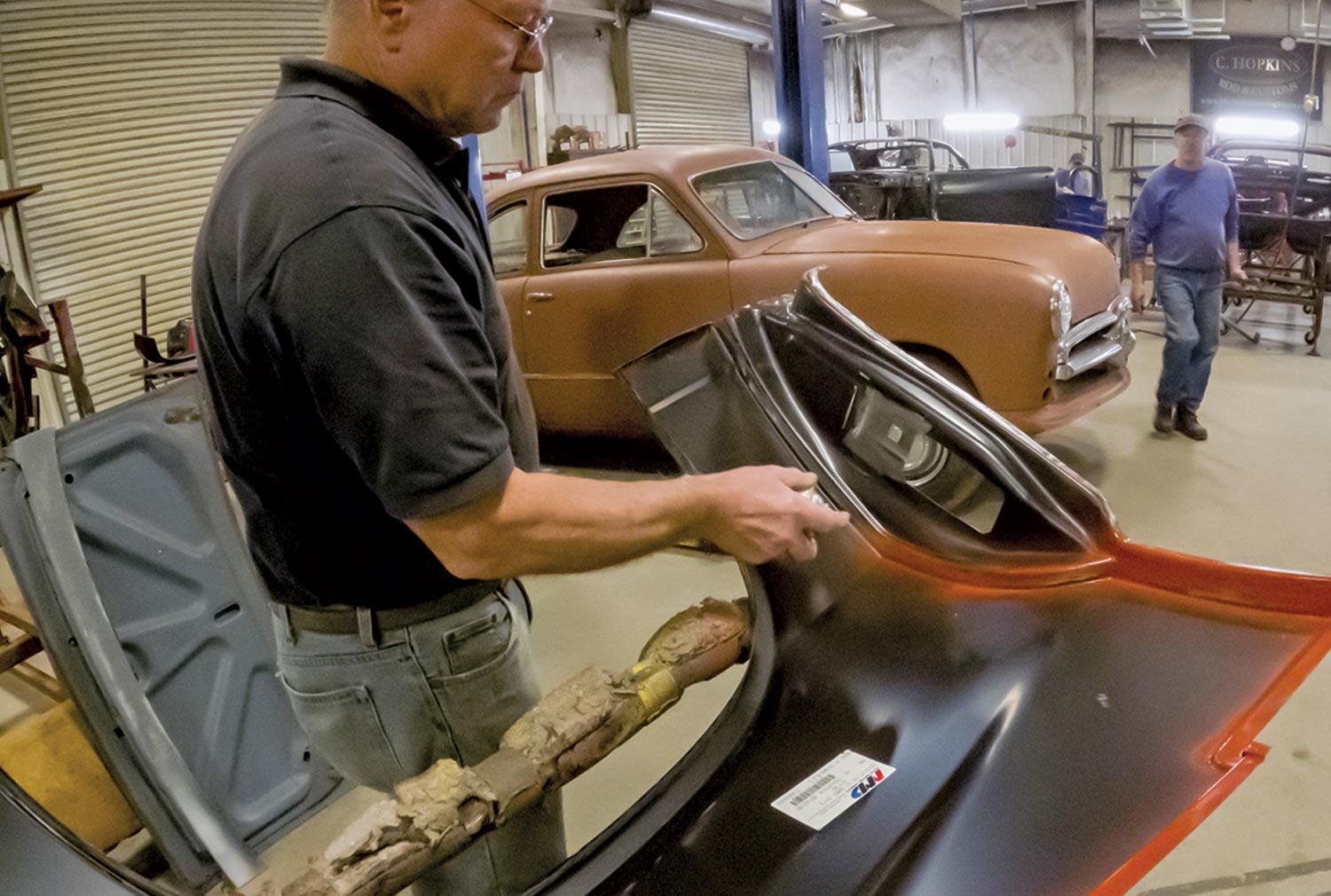 another mechanic applies weld-through primer on a quarter-panel prior to installation