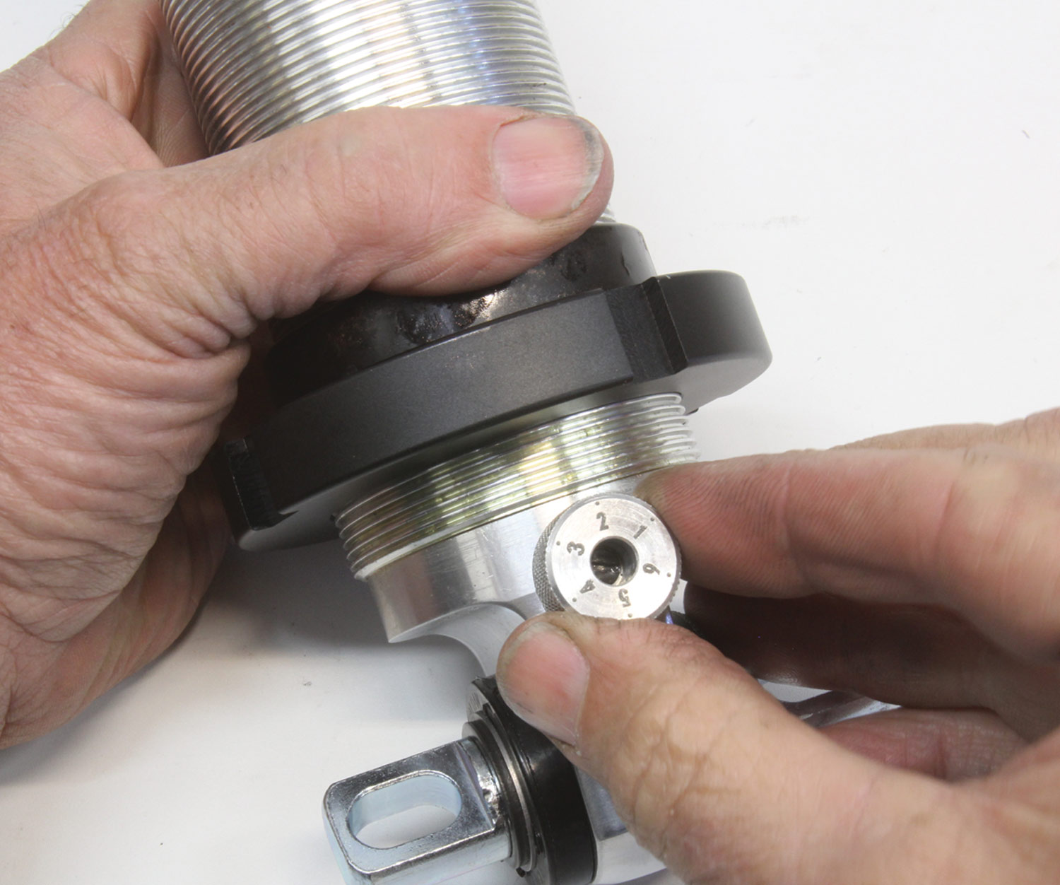 close view of a hand adjusting a single knob at the base of a shock