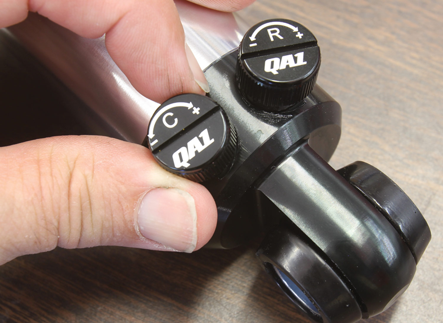close view of two knobs, labeled "C" and "R" at the base of a shock, a hand turns the "C" labeled knob