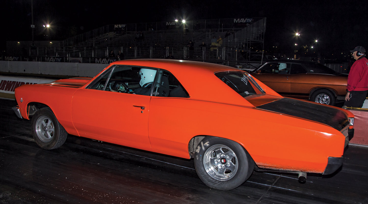 driver side profile view of an orange car at a night drag race