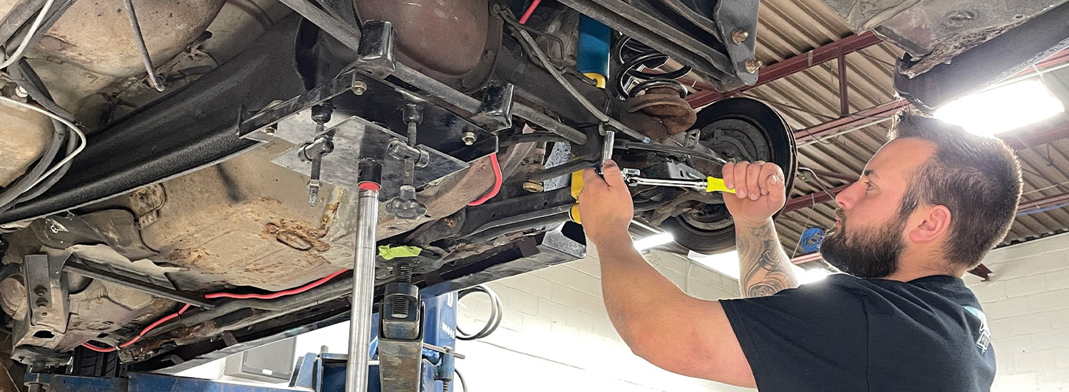 mechanic works on a bolt from the underside of the lifted car