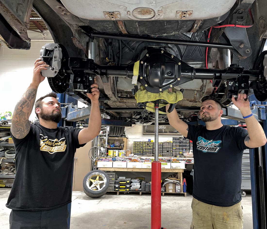 with help, the mechanic raises the newly assembled axle into place on the lifted car