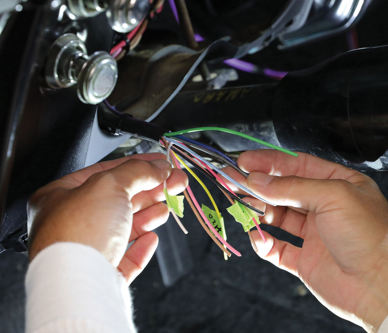 mechanic hands hold the vehicle harness wires labeled with tape strips for organization