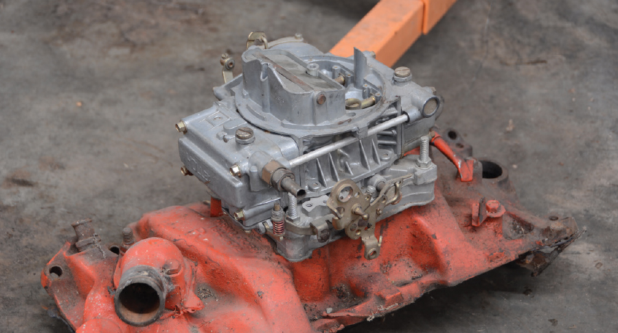 a pile of parts, including a cast-iron four-barrel intake manifold with a semi-modern Holley carburetor