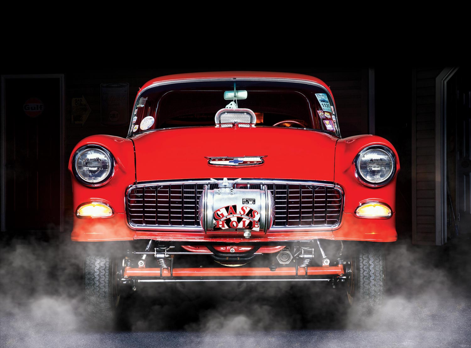 close front view of Garry Gallo's red '55 Chevy gasser, featuring various vintage stickers on the windshield, and a front tank reading "GASS HOLE"