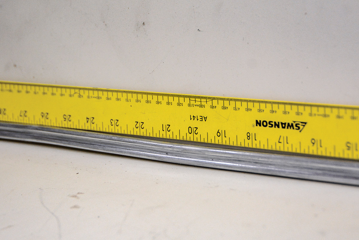 Other types of damage include lateral bends. Sometimes, these types of bends can happen without denting the trim, and it usually happens when someone tries to remove the trim incorrectly. A straightedge is used to determine the low and high spots. We mark the spots that need attention and carefully clamp it in the vise to hand-work the trim.