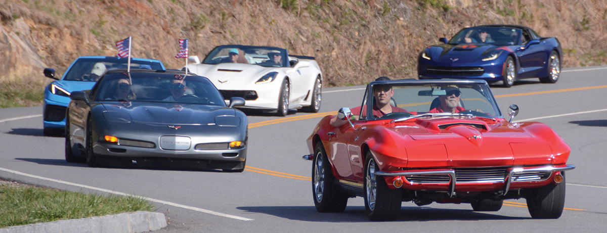 Line of convertible Corvettes driving on windy road