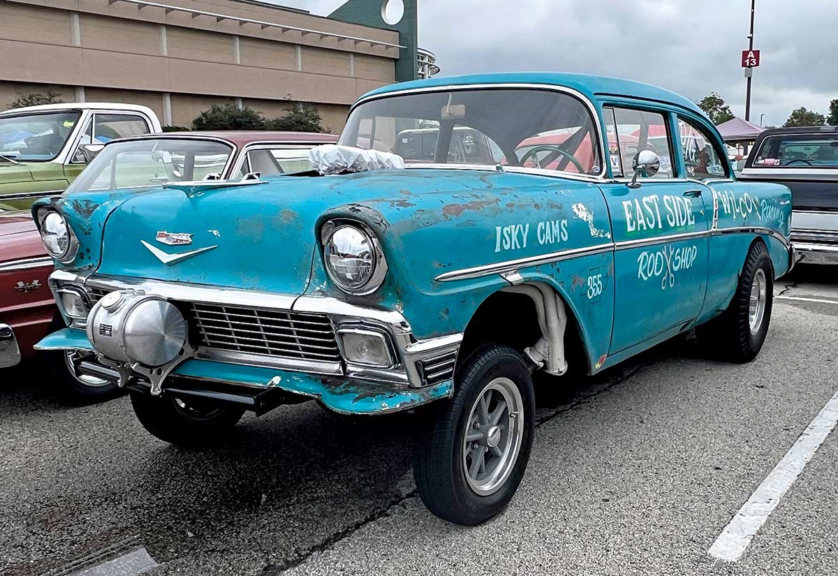 Close-up photograph perspective of a dark marine blue Chevy vintage car "Isky Cams East Side Rod Shop" parked on display at the 54th annual NSRA Street Rod Nationals with other cars nearby in the area