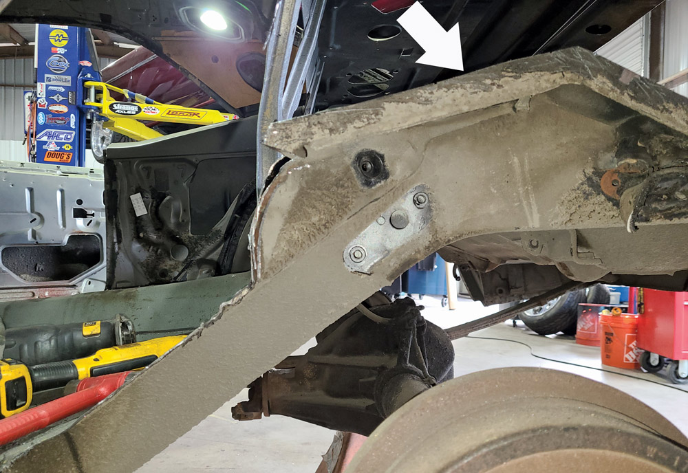  After removing the seat-side section of the floor, this view shows the area around the upper shock mount (arrow) that still needs to be removed.