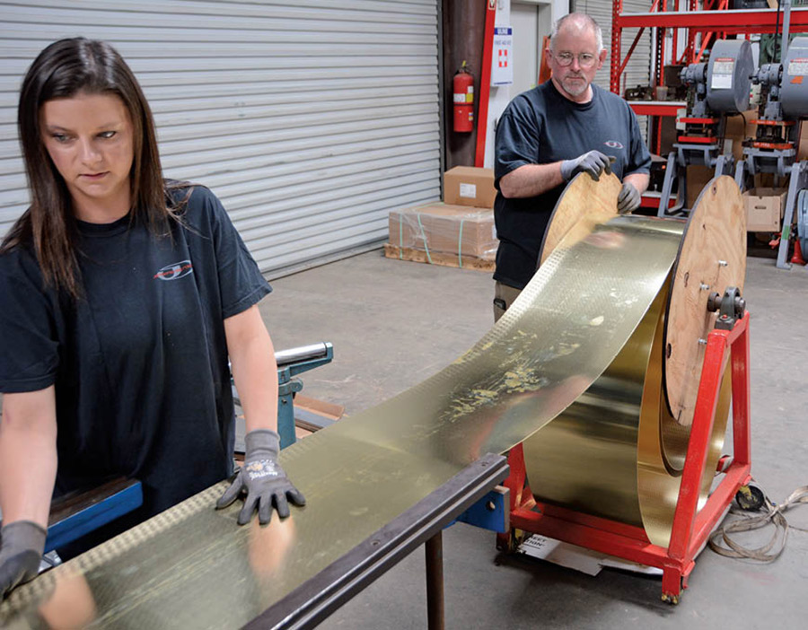 Brittany Winningham steps in to help Jackson feed brass stock into the shear. These pieces are used to fabricate the tanks. For a Tri-Five Chevy radiator, the upper tank is stamped and the lower is cut and formed from one piece of brass.