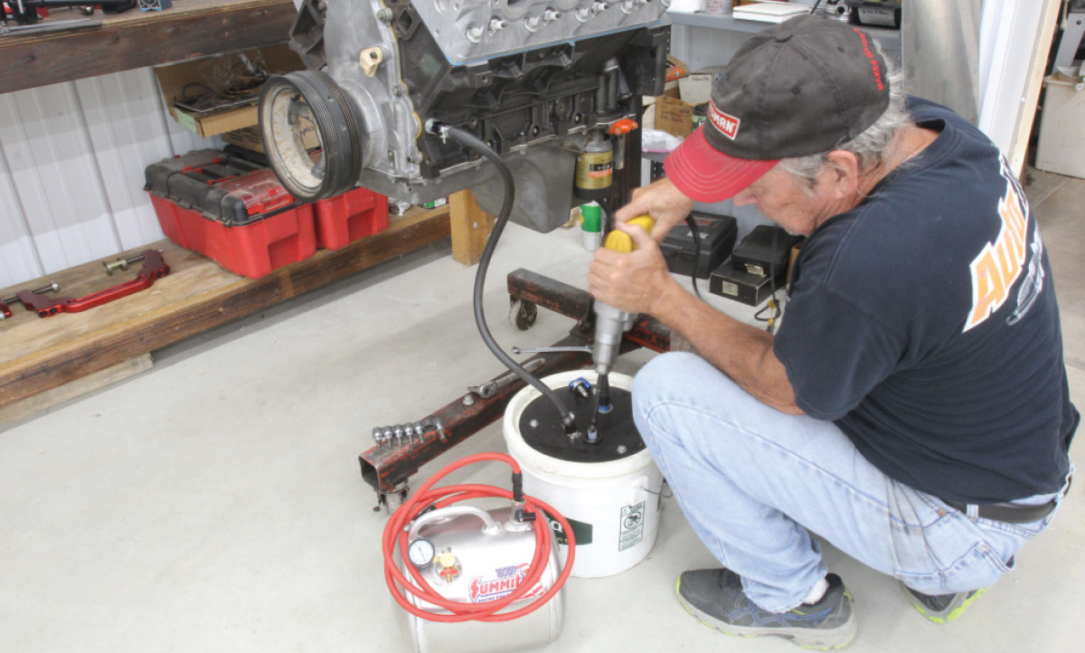 There are several pressure lube tank kits available, including that aluminum pressure feed tank from Summit Racing in the foreground. Many years ago, we built our own pressure luber using a plastic bucket with an aluminum plate to reinforce the lid. Then we bolted a small-block Chevy oil pump to the lid and extended the pickup with a length of 5/8-inch heater hose. We tapped the oil pump output for a -6 AN fitting plumbed to the LS main galley. We also fitted a return from the oil drain plug back to the tank. 