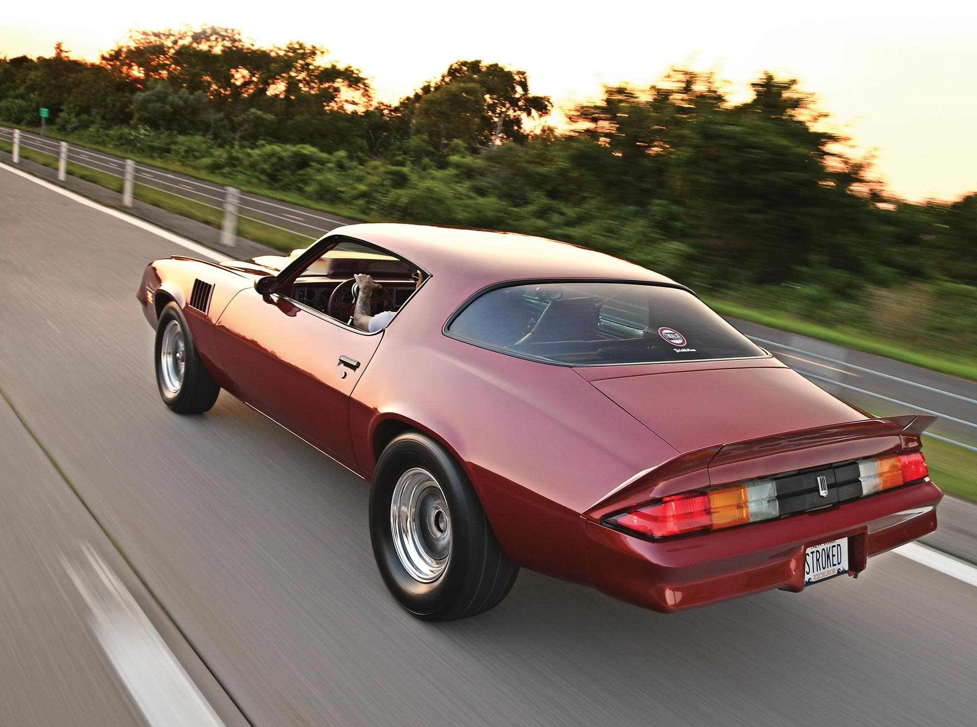 angled 3/4ths rear view of the the Flame Red ’79 Camaro Berlinetta riding up a highway