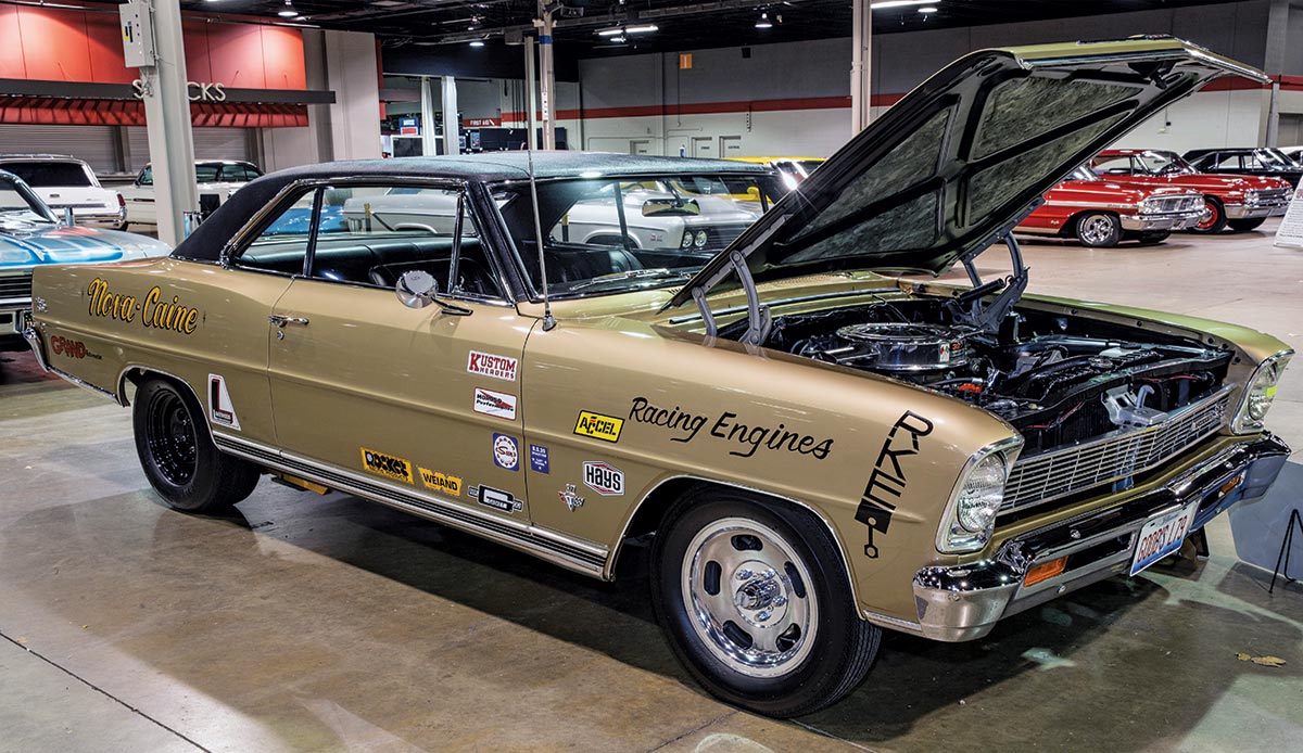 Close-up photograph perspective of a vintage dark gold 1967 Nova SS custom-themed car with its hood open in a display area of a showroom floor