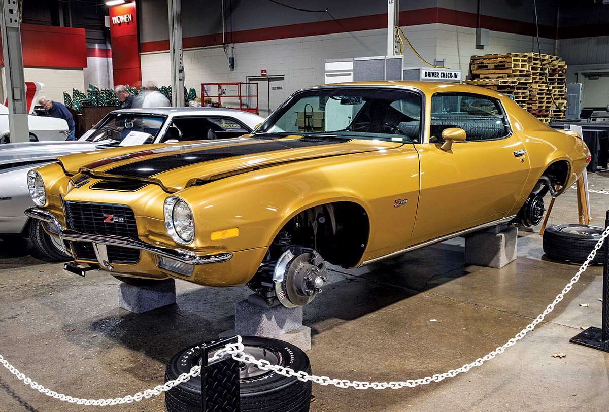 Close-up photograph perspective of a gold/black vintage Camaro muscle car (Z/28 model) on top of grey cushion bricks without no tires installed in a display area of a showroom floor