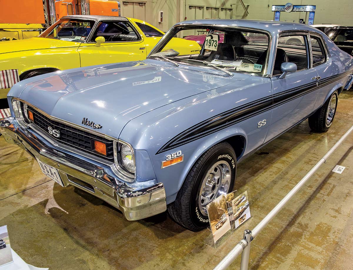 Close-up photograph perspective of a vintage faded blue/black Chevy Nova muscle car (SS 350 model) in a display area of a showroom floor