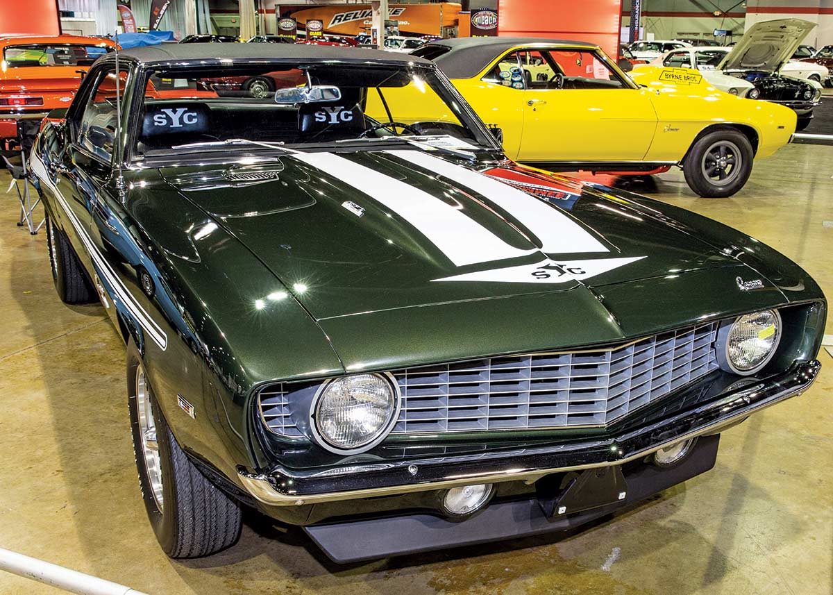Close-up photograph perspective of a vintage dark forest green/white Camaro muscle car in a display area of a showroom floor
