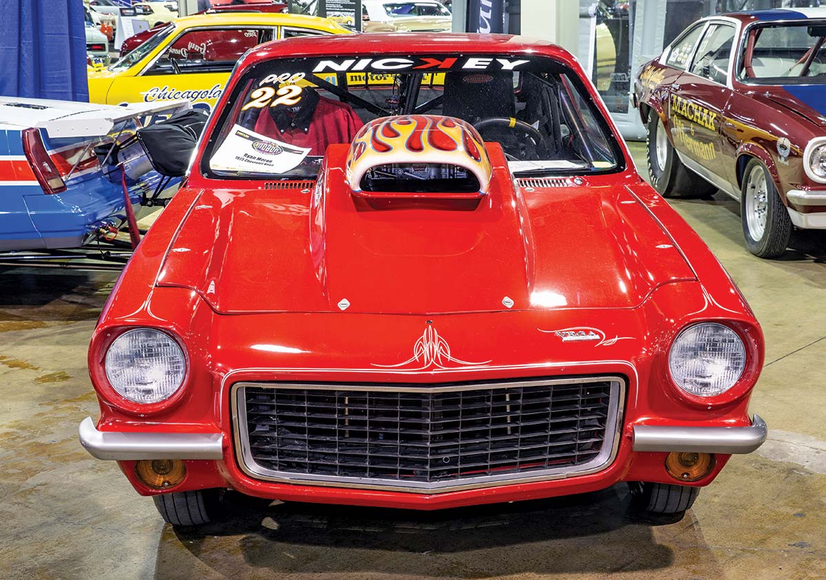 Close-up photograph perspective of a vintage red/white 1967 Camaro muscle car custom-themed model named Pro 22 Nickey in a display area of a showroom floor