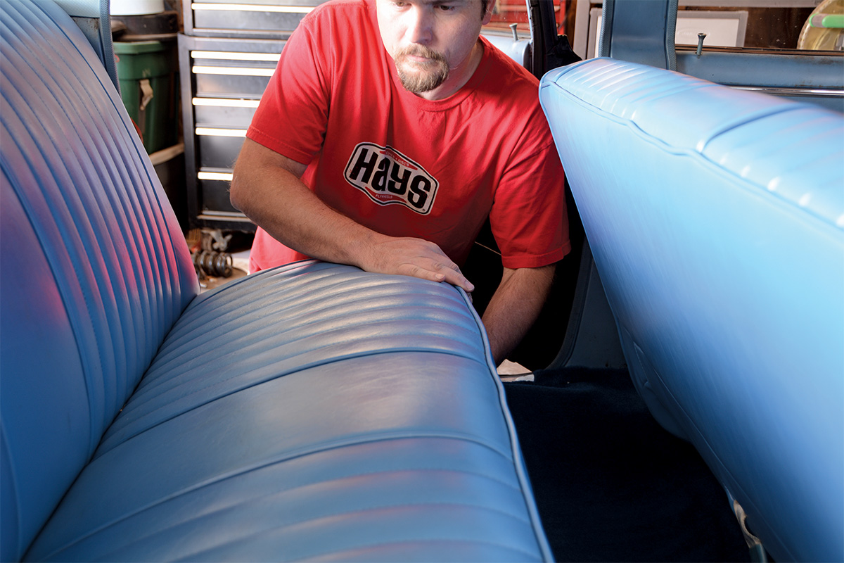 Man in red shirt looking at the blue back seat of a car
