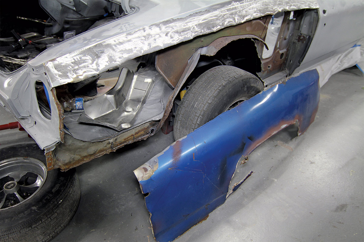 Rusty blue quarter panel, sitting on ground and leaning against wheel well of car