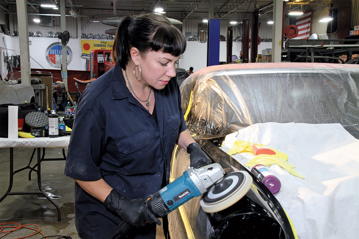 Woman in blue jumpsuit, buffing the front of a car