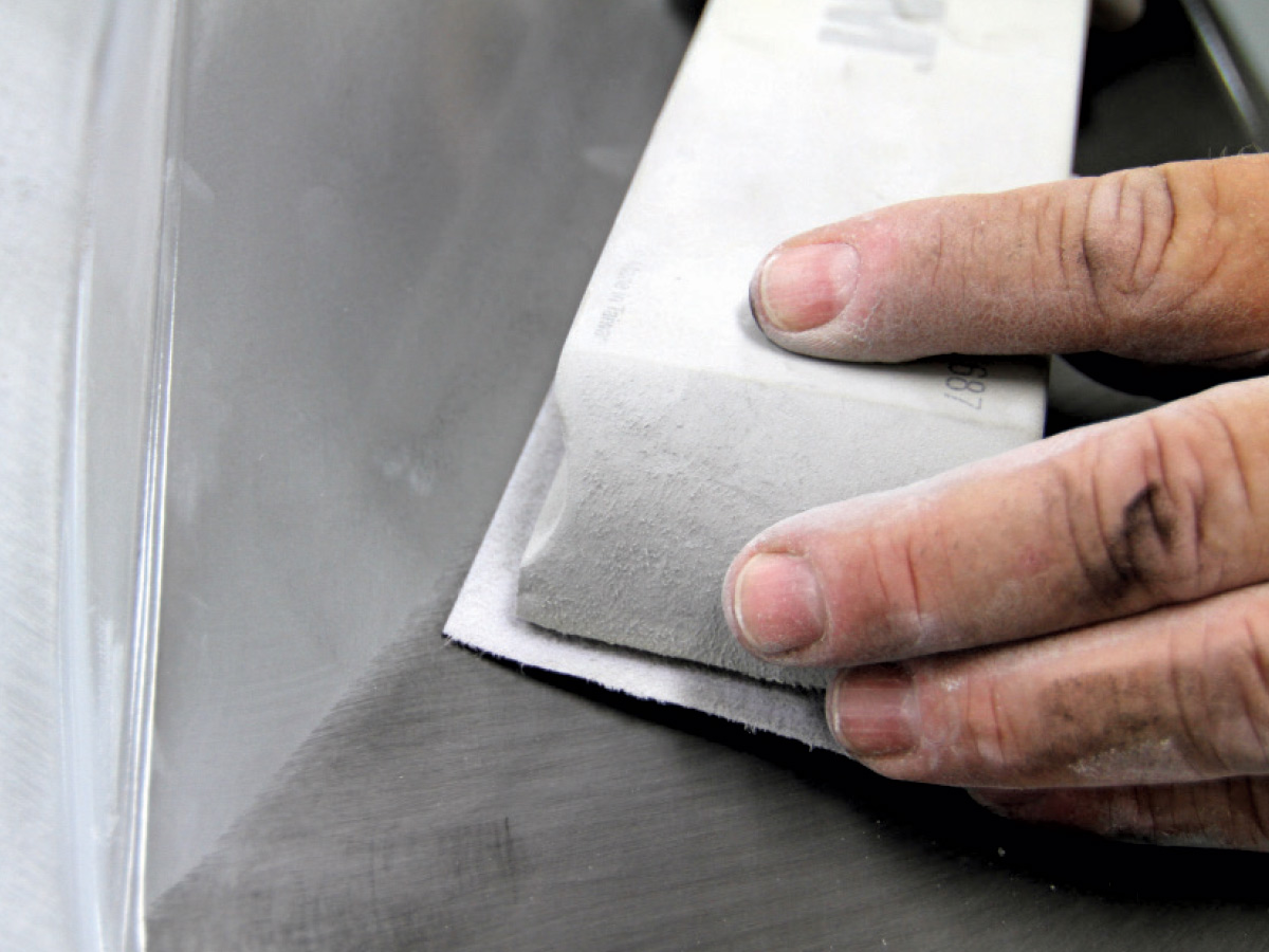 Hands using a large white sanding block with a piece of 220-grit paper attached