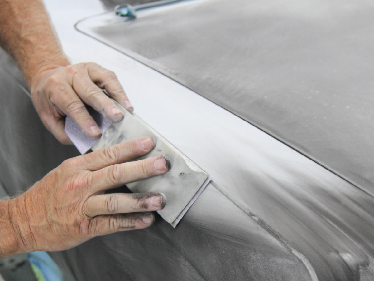 Hands using a sanding block on the edges of a car