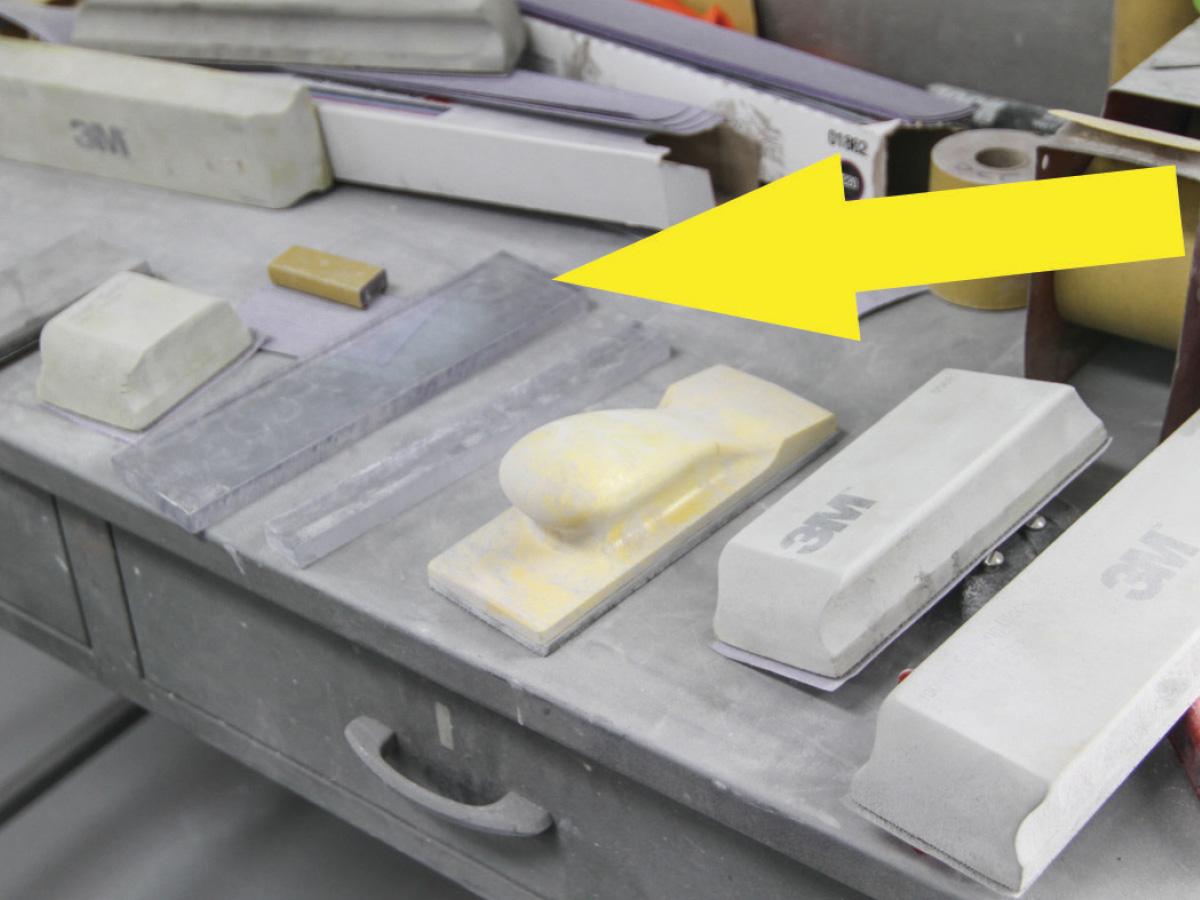 Different sized sanding blocks laid out on a grey work station and a yellow arrow graphic pointing at blocks made of polycarbonate