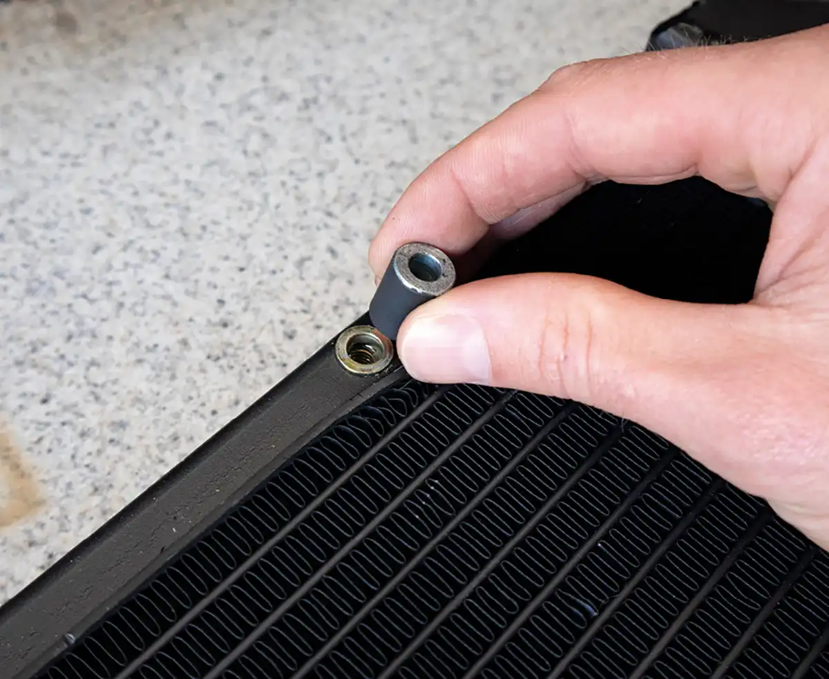 To actually mount the Vintage Air fan shroud assembly and lower block-off plate, we installed rivet nuts in the top and bottom of the radiator core frame and then used standoffs to get the spacing right.