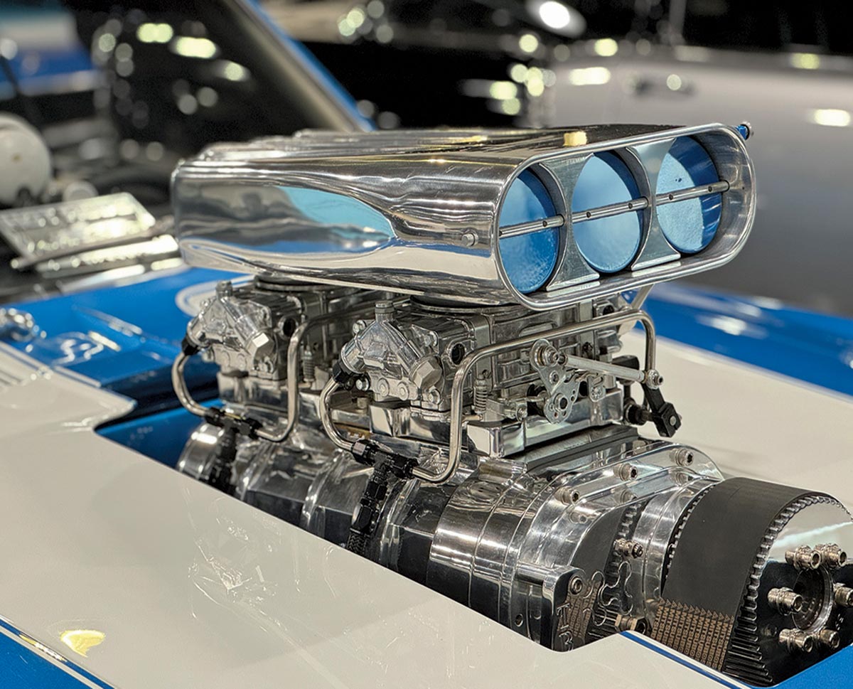 Landscape close-up angle photograph view of a main engine part exposed inside the vintage blue 1969 Chevy Camaro Z/28 model car on the front top hood inside The Grand National Roadster Show (GNRS) showroom venue