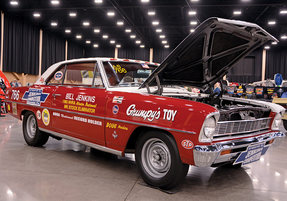 red car with white roof and various word decals parked indoors with its hood open 