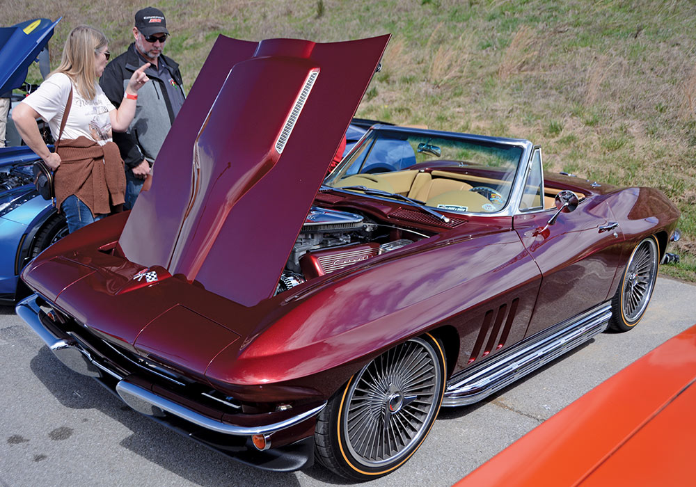 a man and woman standing next to a maroon car with hood open 