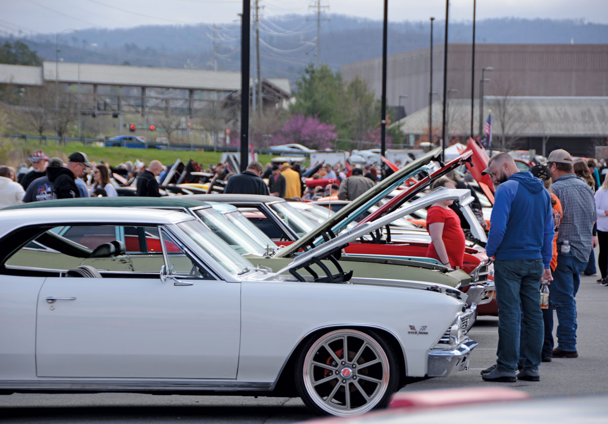 crowd of people looking at the engine of different cars with their hoods open