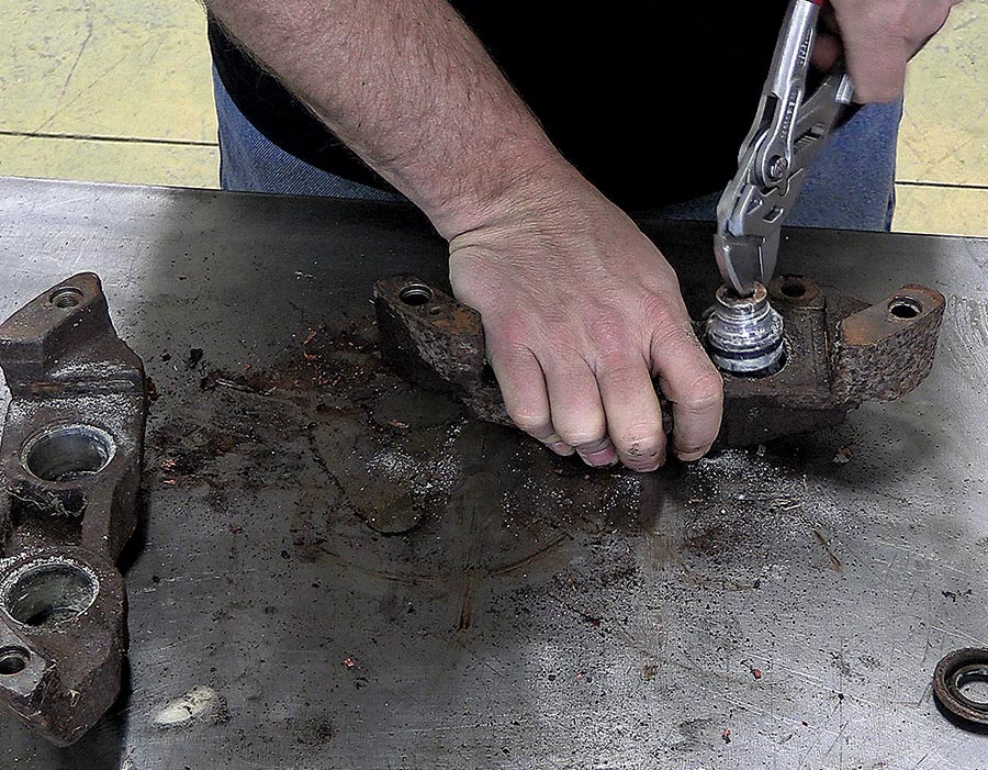 hands using jaw pliers to pull out pistons covered with dried out brake fluid