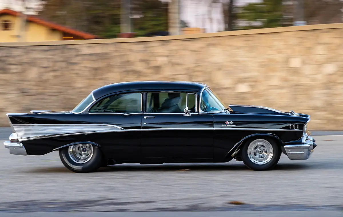 passenger side profile of the black ’57 Chevy 210 riding down a road
