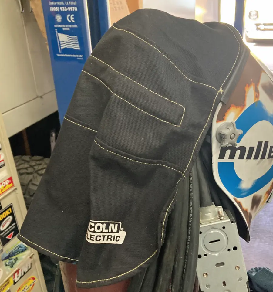 back view of a white and light blue accented helmet from the Miller Digital Infinity series with a rear extension attached to prevent any transient light from ruining the workpiece view