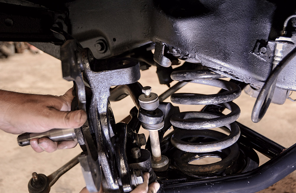 A floor jack is used to raise the lower control arm and compress the spring