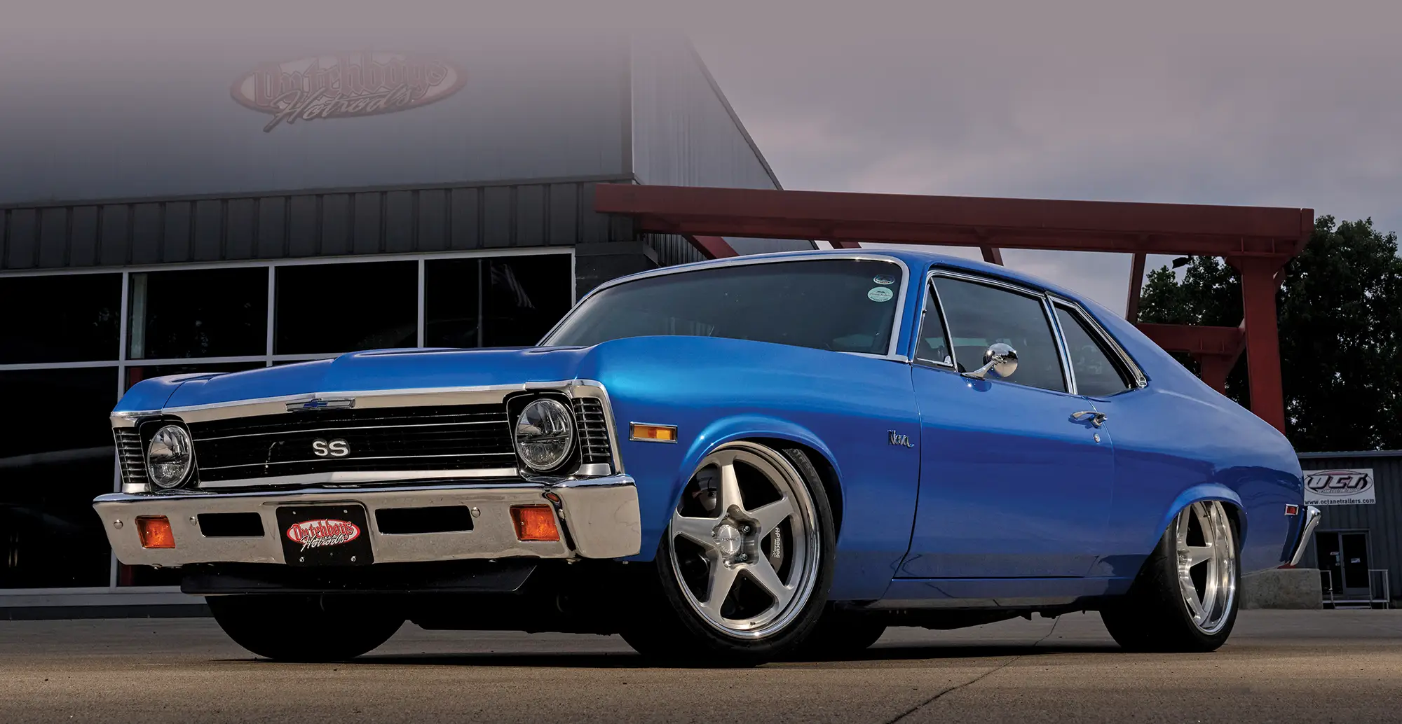 Low-angle shot of a 1971 Chevrolet Nova SS in blue, captured at dusk outside a garage