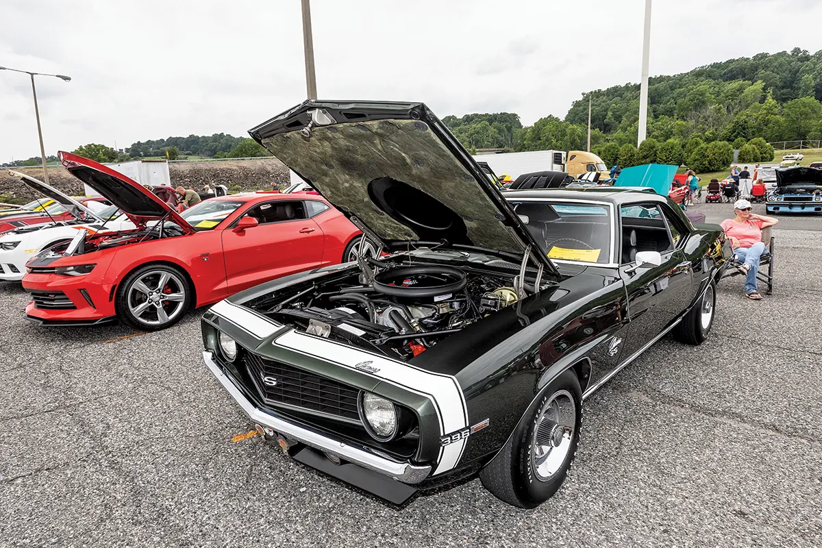 A green 1969 Camaro SS with white racing stripes, parked next to modern Camaros