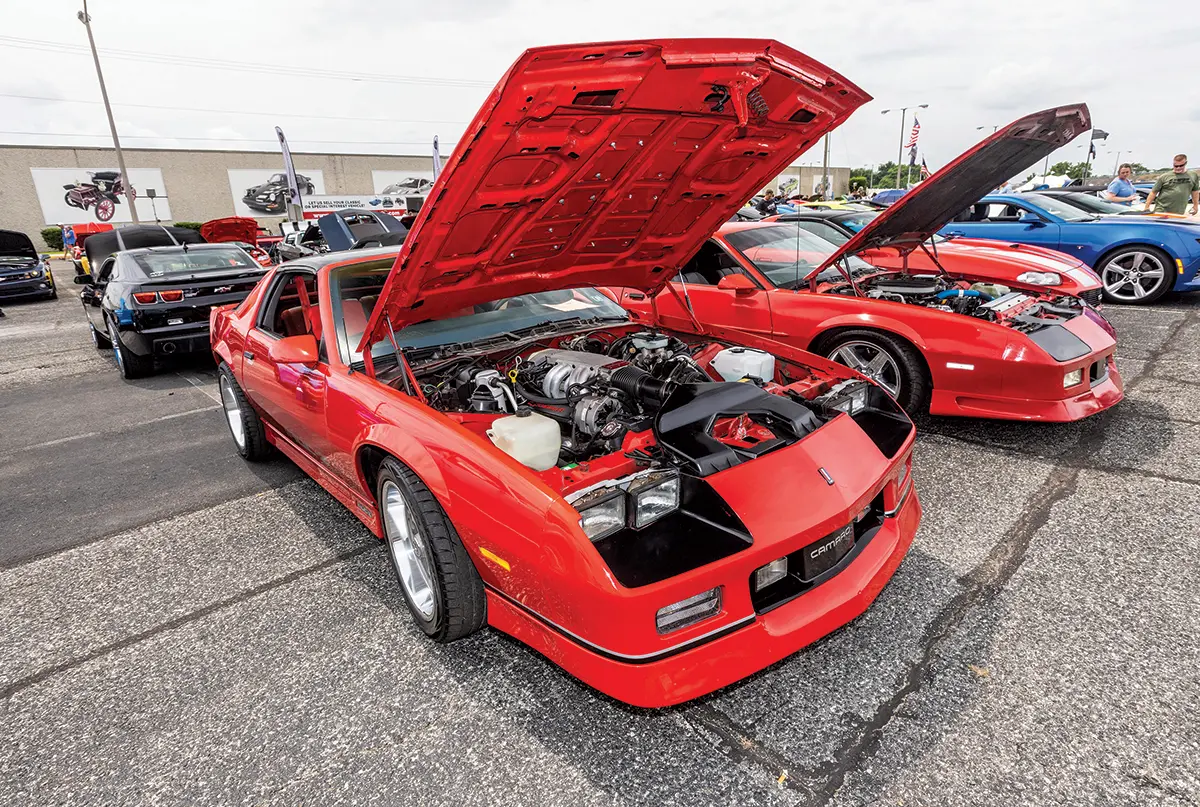 A red third-generation Camaro with its hood up, revealing a detailed engine bay