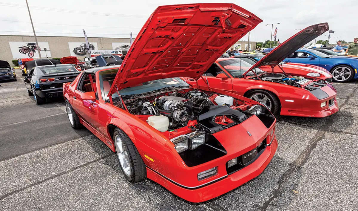 A red third-generation Camaro with its hood up, revealing a detailed engine bay