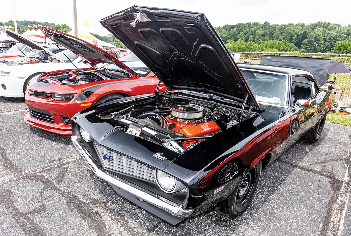 A black 1969 Camaro with a bright orange engine displayed, parked next to modern muscle cars