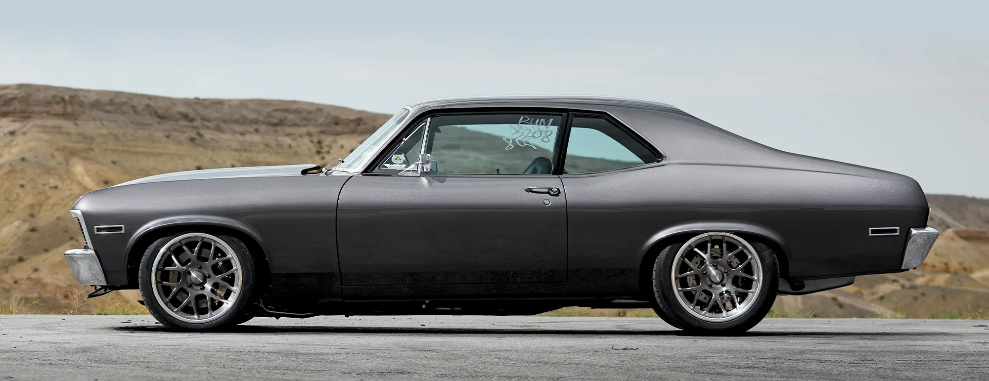 Side profile of a 1971 Chevrolet Nova, highlighting its dark gray finish and modern wheel setup