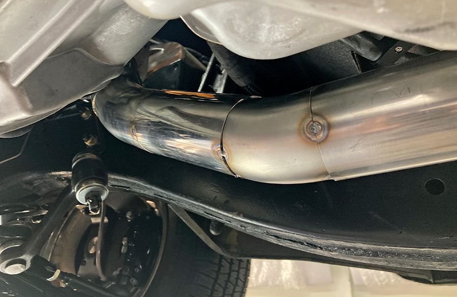 Newly welded stainless exhaust pipe fitted under the vehicle, showcasing clean welds