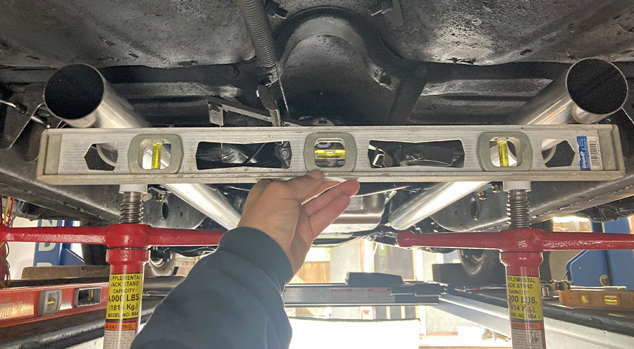 Ensuring exhaust pipes are level using a bubble level during the final fitment under the 1957 Chevy